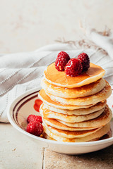 Pancakes poured with honey decorated with raspberries on a plate on a beige background. Copy space
