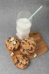 Fresh organic homemade cookies with chocolate chips and dried berries on wooden board with glass of milk on table