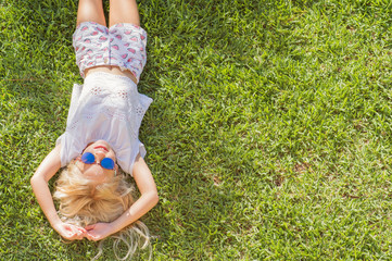 Summertime fun. cheerful girl in sunglasses lying on the grass in the park. child outdoors. vacation in the summer park. top view
