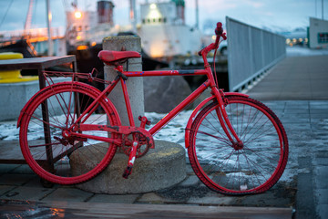 Fototapeta na wymiar Ein rotes Fahrrad mit plattem Reifen lehnt an einem Poller in einem Hafen-Konzept Verlassen, Einsam
