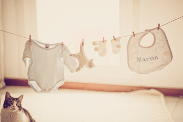 Newborn baby clothes hanging inside the house with cat watching.