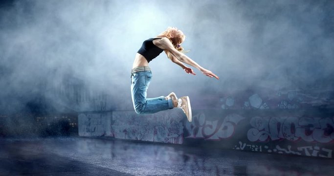 Female street dancer in a jump with a graffity wall behind the fog on a backgroung.