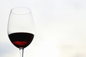 Close-up of a glass glass of red wine against a blurred background of the sky and sunset in the evening. Concept of romantic holidays