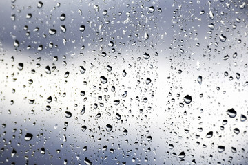 Drops of morning summer rain on the transparent window of the house on a blurred background of nature. Summer vacation and travel concept