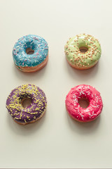 assorted donuts of different colors such as pistachio, blue, pink and bilberry with frosted and filled with fruit cream and jam, colored glazed and sprinkled donuts on yellow background, top view