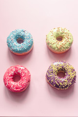 closeup of assorted donuts of different colors such as pistachio, blue, bilberry and strawberry with frosted and filled with fruit cream and jam, colored glazed and sprinkled donuts on pink background