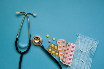 Stethoscope, pills and mask on blue background.