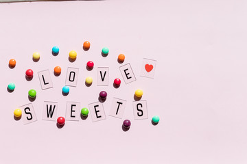 Assortment of sweet candies on pink background.colorful candies and text love sweets.Flat lay composition with jelly beans. Colorful chocolate candies.chocolate buttons