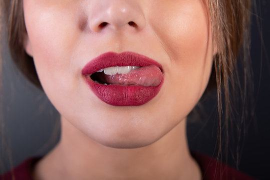 Open female mouth. Sexy lips with tounge of young woman over gray background, face detail. Temptation, appetite, sexuality theme. Girl licks