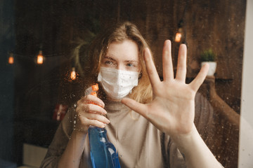Woman with big sanitizer standing near the window in quarantine time