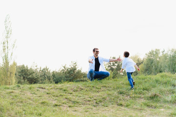 Naklejka na ściany i meble Handsome dad with his little cute son are having fun and playing on green grassy lawn. Happy family concept. Beauty nature scene with family outdoor lifestyle. family resting together. Fathers day