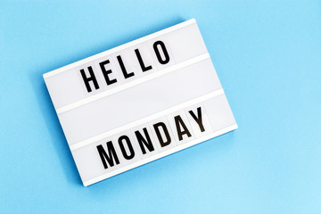Text "hello monday" on lightbox for holiday - Thank God It’s Monday. Start of working week concept. Top view on blue background.