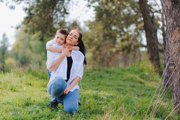 Fototapeta premium Happy young mother is playing with her baby in a park on a green lawn. Happiness and harmony of family life. Great family vacation. Good weekend. Mothers Day. Holiday. The concept of a happy family