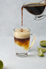 Making tonic coffee cocktail with lime on light backgound. Coffee is pouring into tall glass cup with tonic. Copy space.