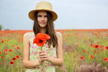 Young beautiful woman walking at poppy field. Happy girl enjoing life among blooming red flowers, summer nature outdoor