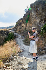 Georgia, Tbilisi - October 21, 2019: Attractive beautiful young girl who is female photographer traveller holding modern mirror camera in the hands outdoors in the mountains