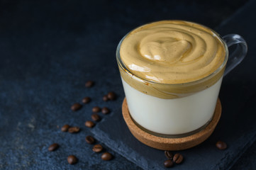 Dalgona coffee in glass cup with coffee beans on dark stone background. Copy space. Homemade Dalgona foam with Sugar, instant coffee and hot water. Whipped Trendy Korean Coffee.