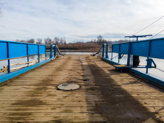Obraz premium Ferry for transporting goods and people across the river moored along the river bank with a lowered ramp ready for loading. Raft made of metal with metal fences and wooden floor.