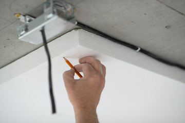 Styrofoam, seiling mounting. A man marks with pencil a cut on the foam. Ceiling insulation. Warming. Repair in the house. DIY repair