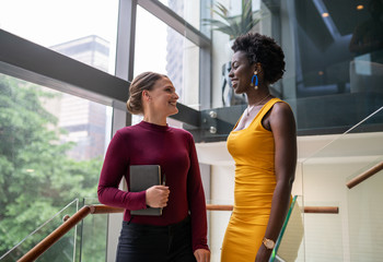 Two smiling young businesswomen talking on some office stairs