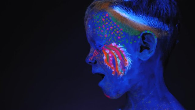The body art on the little boy's body glows in ultraviolet light. Portrait of a small child with an ultraviolet pattern on the face that glows under fluorescent lighting.