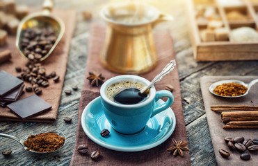 Obraz na płótnie Canvas A cup of aromatic black coffee, a coffee maker, coffee beans of different varieties on the table. Morning espresso or Americano coffee for breakfast in a beautiful brown cup.
