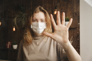 Woman in mask at quarantine with toilet paper standing at the window isolated