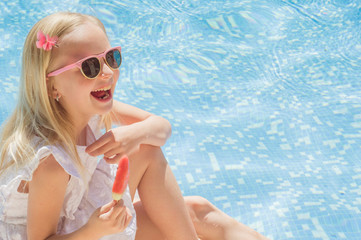 Summertime fun. Happy little girl eating ice cream near the pool
