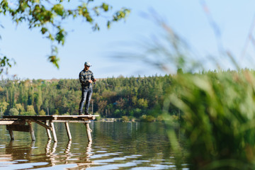 Obraz premium Fishing in river.A fisherman with a fishing rod on the river bank. Man fisherman catches a fish pike.Fishing, spinning reel, fish, Breg rivers. - The concept of a rural getaway. Article about fishing.
