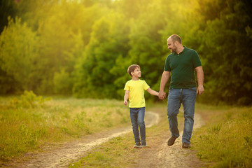 A happy family. father and son walk along the road and hold hands for a walk in the forest.