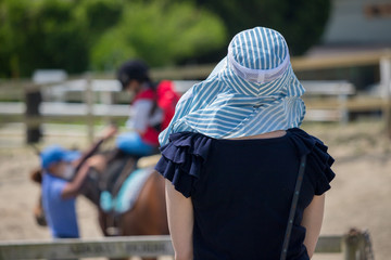 乗馬体験している子供を見ている母親