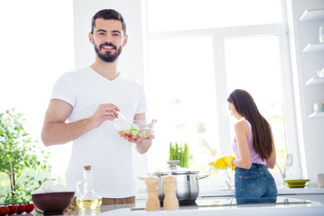 Idyllic family portrait concept. two people stay home kitchen man mix salad spoon bowl his wife wash plate in yellow rubber latex gloves sponge after romantic dinner in house indoors