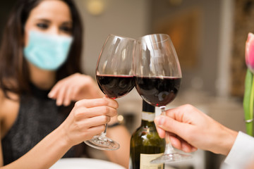Masked couple toasting wineglasses in a restaurant during coronavirus pandemic