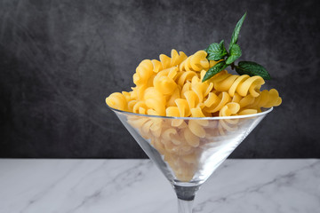 Raw uncooked italian pasta on cocktail glass over white marble. Fusilli. Diet and food concept. Copy space. Close up.
