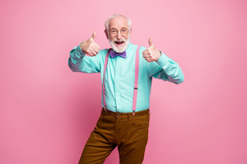 Portrait of positive cheerful old man promoter show thumb-up sign suggest select ads promotion wear turquoise pants isolated pastel pink color background