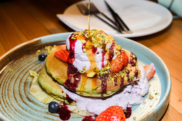 Matcha powder pancakes served in a restaurant setting, with ice cream, strawbberries and chocolate