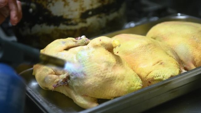 Un cuisinier br&ucirc;le la peau de la volaille au chalumeau