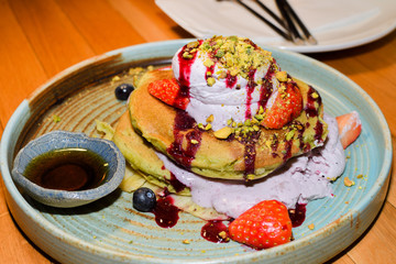Matcha powder pancakes served in a restaurant setting, with ice cream, strawbberries and chocolate