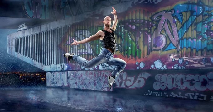 Male street dancer in a jump with a graffity wall on a backgroung.