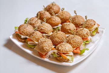 Mini chicken burgers with cheese and tomatoes on a white plate. Bonded with beautiful bamboo sticks.