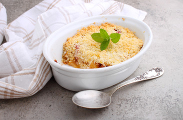 Crumble with strawberries and apples on a white plate and concrete background.