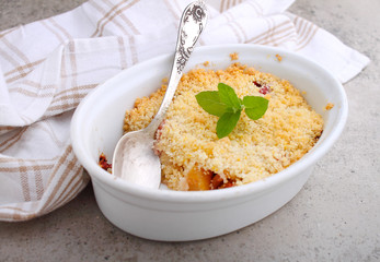 Crumble with strawberries and apples on a white plate and concrete background.