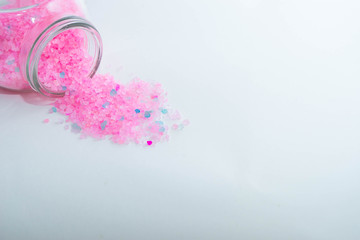 Close-up on upper part of jar with light pink bath salts are on the left upper corner of the frame. Horizontal photo. Object on a white background. Banks are lie on its side. Bath salt spilled out
