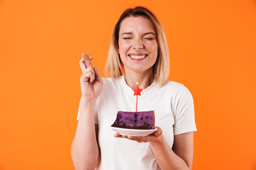 Image of excited woman with fingers crossed holding cake with candle