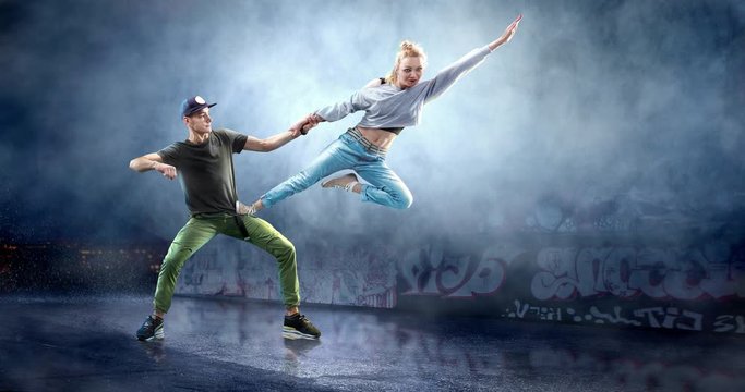 A couple of street dancers in a action with a graffity wall behind the fog on a backgroung.