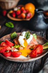 poached egg with vegetables, avocado, salmon and herbs in bowls on brown wooden table, healthy breakfast concept