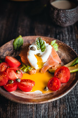 poached egg with vegetables, avocado, salmon and herbs in bowls on brown wooden table, healthy breakfast concept