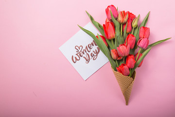 red  beautiful tulips in an ice cream waffle cone with card Womans Day on a color background. Conceptual idea of a flower gift. Spring mood