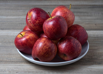 Plate with fresh ripe red apples on wooden background.