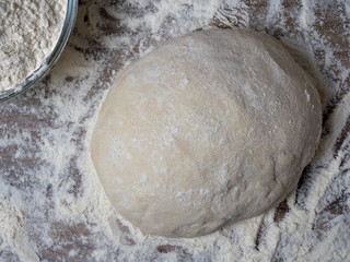 Raw dough covered with flour on a wooden background.